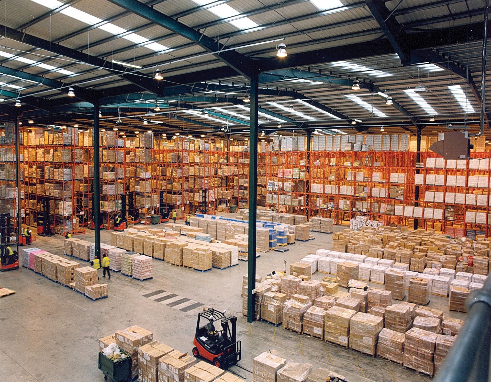 Tall pallet racking filled with stored goods running down the aisles of a modern warehouse.