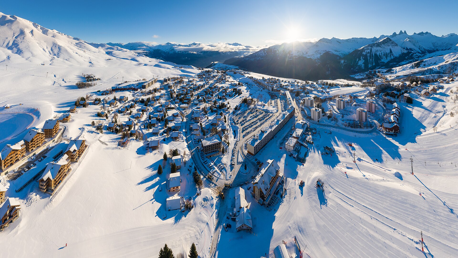 A snow-covered ski resort town with runs and lifts spreads across a mountain valley at sunrise.
